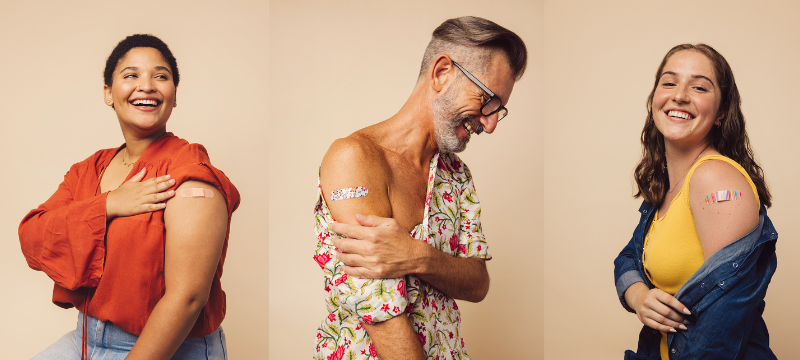 Two young women and a middle-aged man with rolled up sleeves, showing off their freshly-vaccinated shoulders.