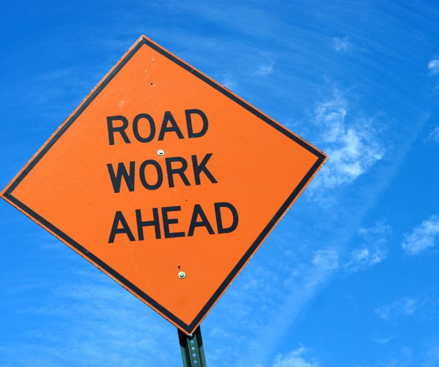 Orange sign reading road work ahead against blue sky
