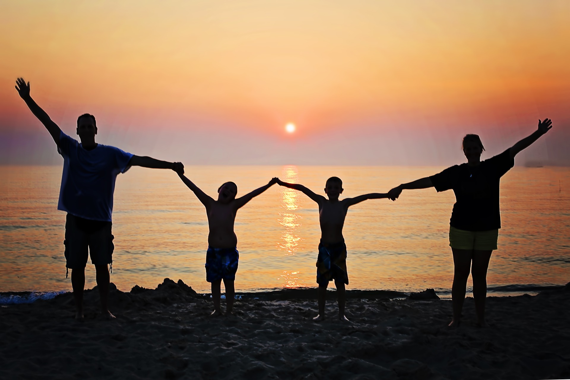 Family with arms raised, holding hands in front of ocean at sunset