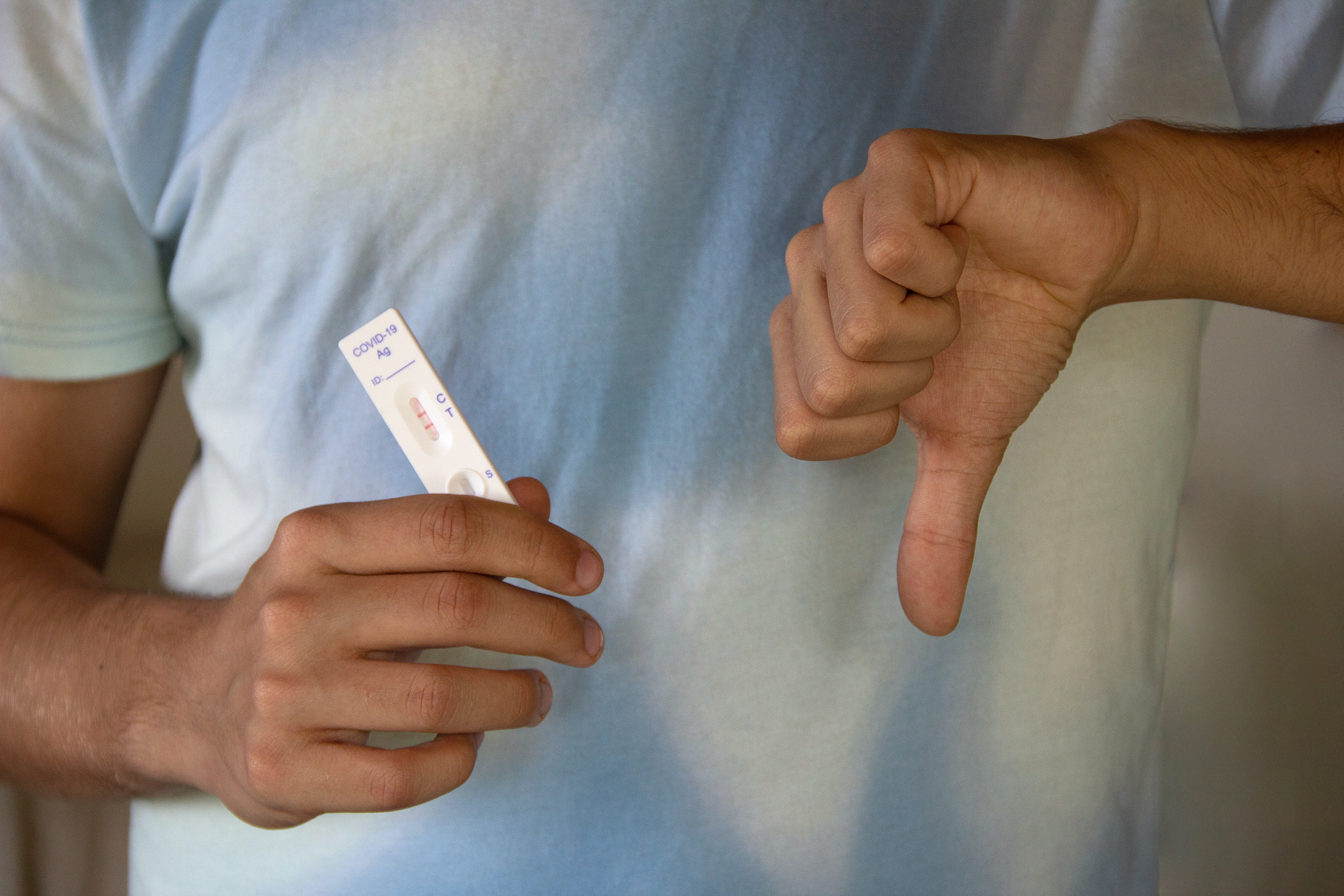 Person holding a COVID-19 Rapid test with a thumbs down indicating they tested positive.