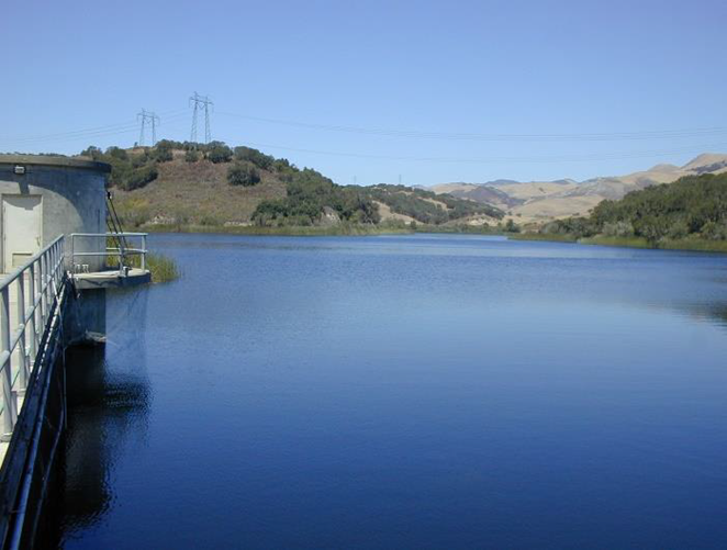 Overlooking reservoir with blue water, metal walkway to the side, and mountains in background