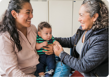 Mom is holding baby and grandma is holding baby's hand