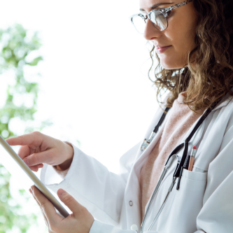 Young woman doctor with curly brown hair and glasses reading from a tablet device.