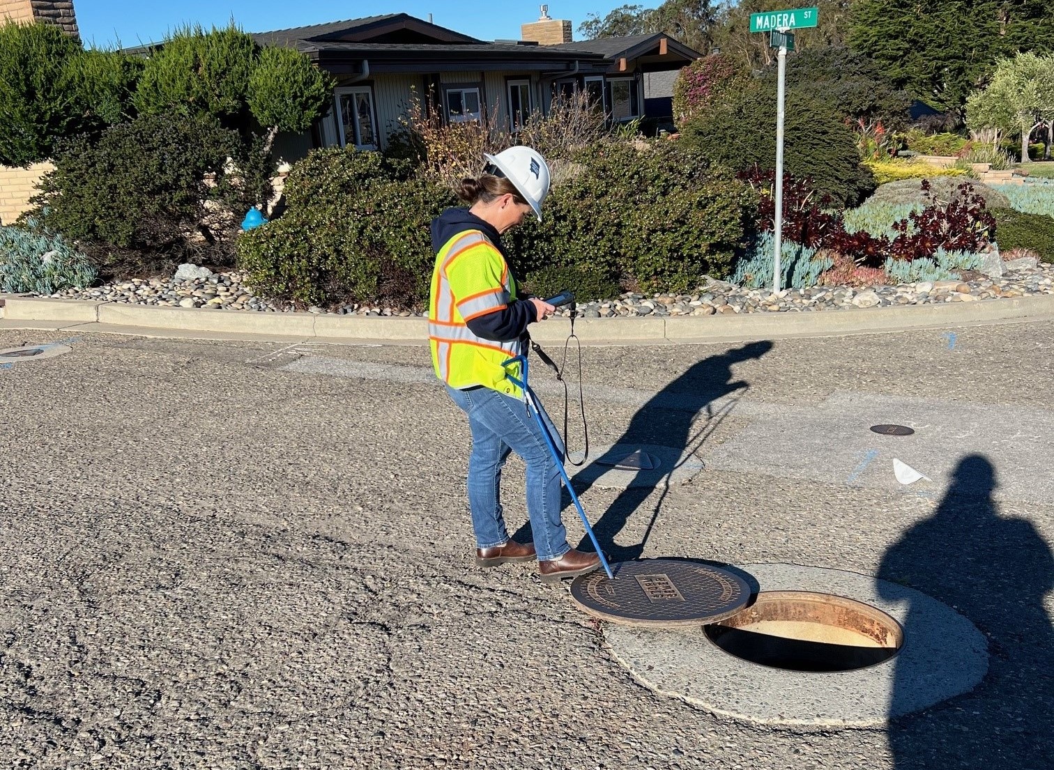 A person wearing a safety vest standing over open drain