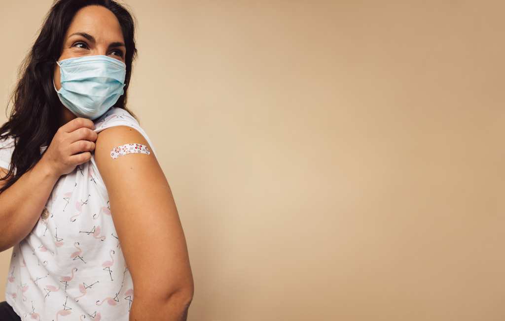 Woman wearing a mask and showing off a bandaid.