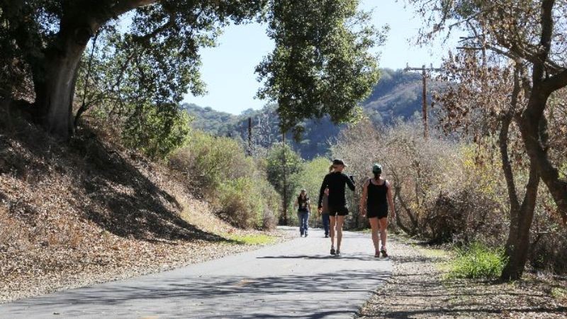 Two women walking on the sunny lit Bob Jones Trail surrounded by trees