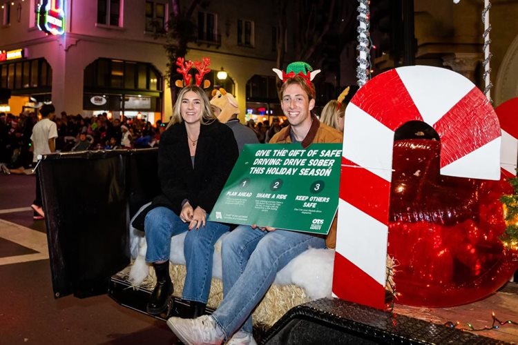 Woman and man riding a parade float holding signs encouraging driving sober.