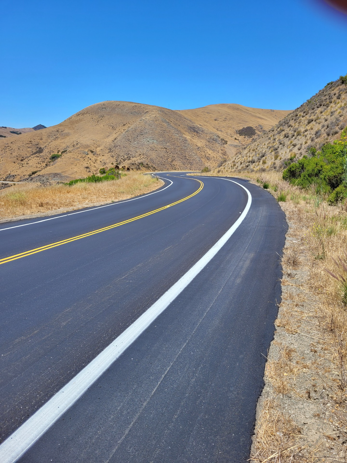 Image of a recently repaved road curving before disappearing between two hills.